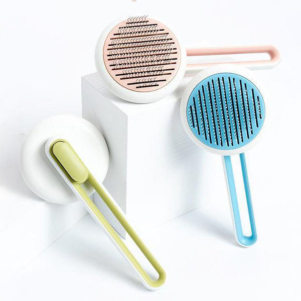 Three modern pet deshedding brushes in pink, blue, and green arranged on a white geometric background.