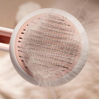 Overhead close-up of a circular pet brush with angled metal bristles holding a large amount of shed white fur.