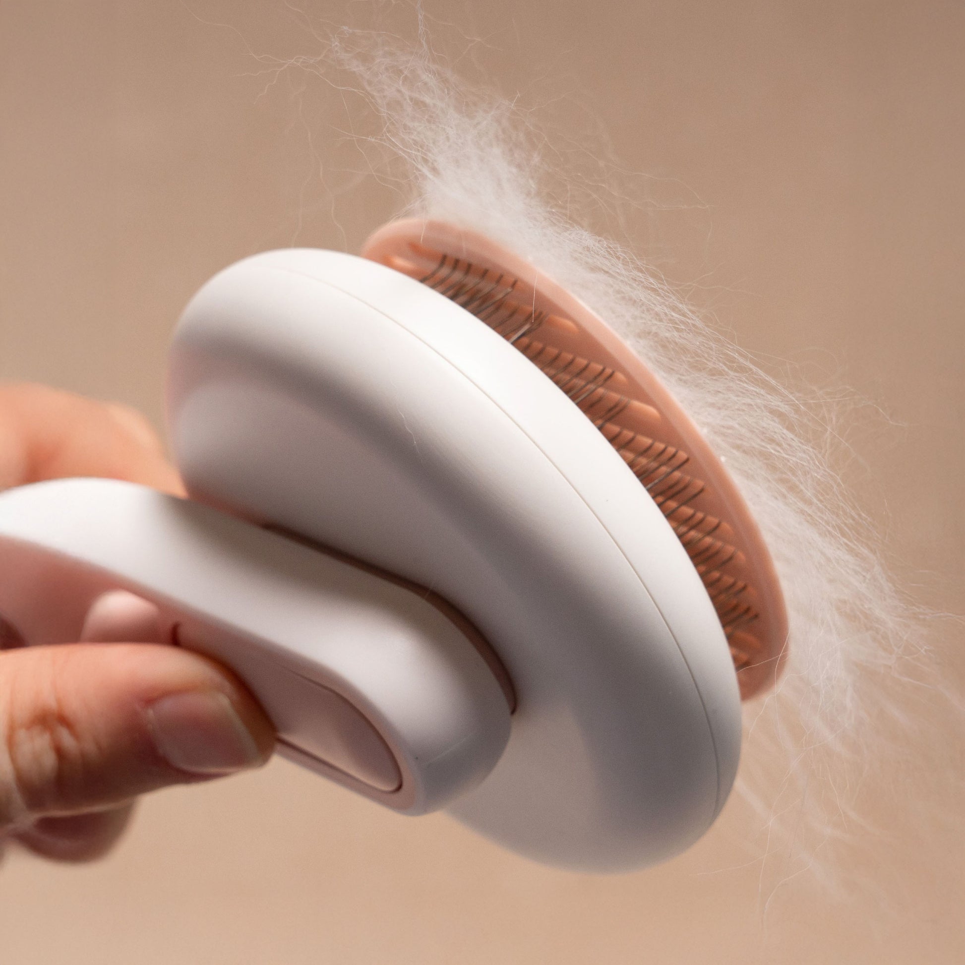 Side view of a hand holding a white and pink self-cleaning pet brush showing the curved metal bristles full of white cat fur.